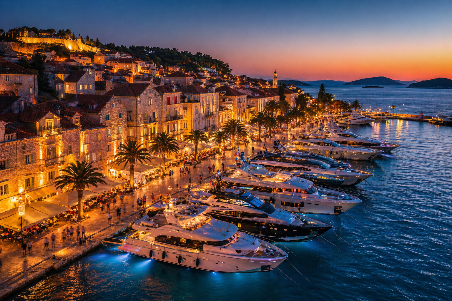 Aerial view of a vibrant Croatian harbor town at night with luxury yachts moored at the waterfront during peak summer season.