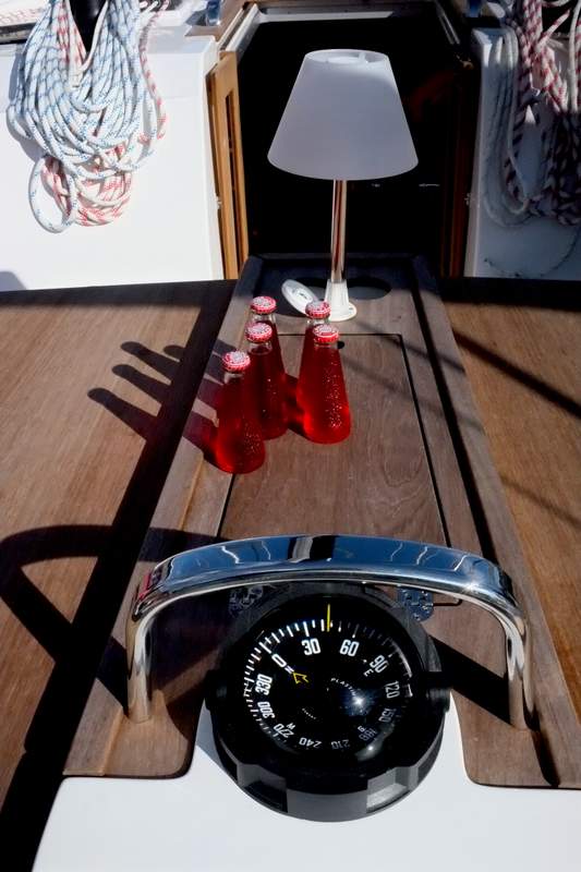 Sibylla's polished helm with navigation instruments and stylish red drink cups on deck.