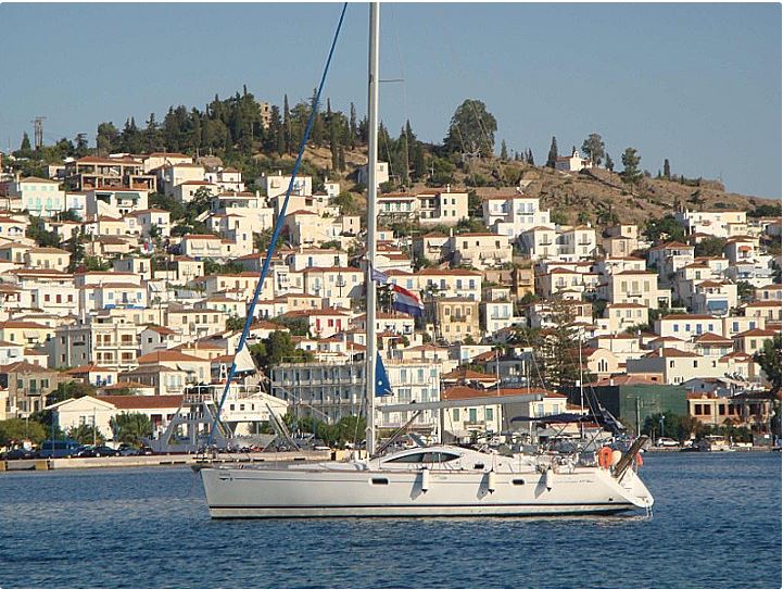 Idrea gracefully sailing past a picturesque coastal town, showcasing its elegant profile and pristine hull.