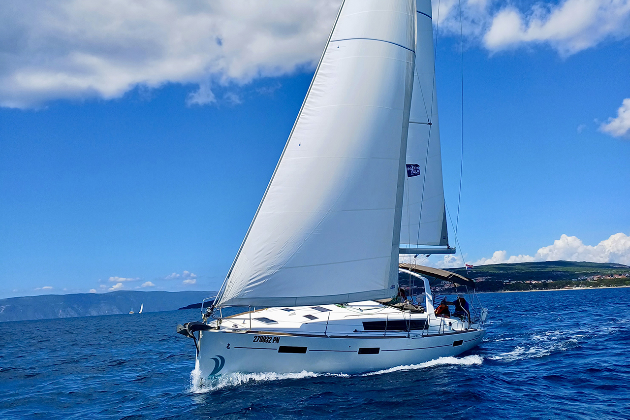 Sleek profile of the Buddy sailing gracefully on azure waters under a clear sky.