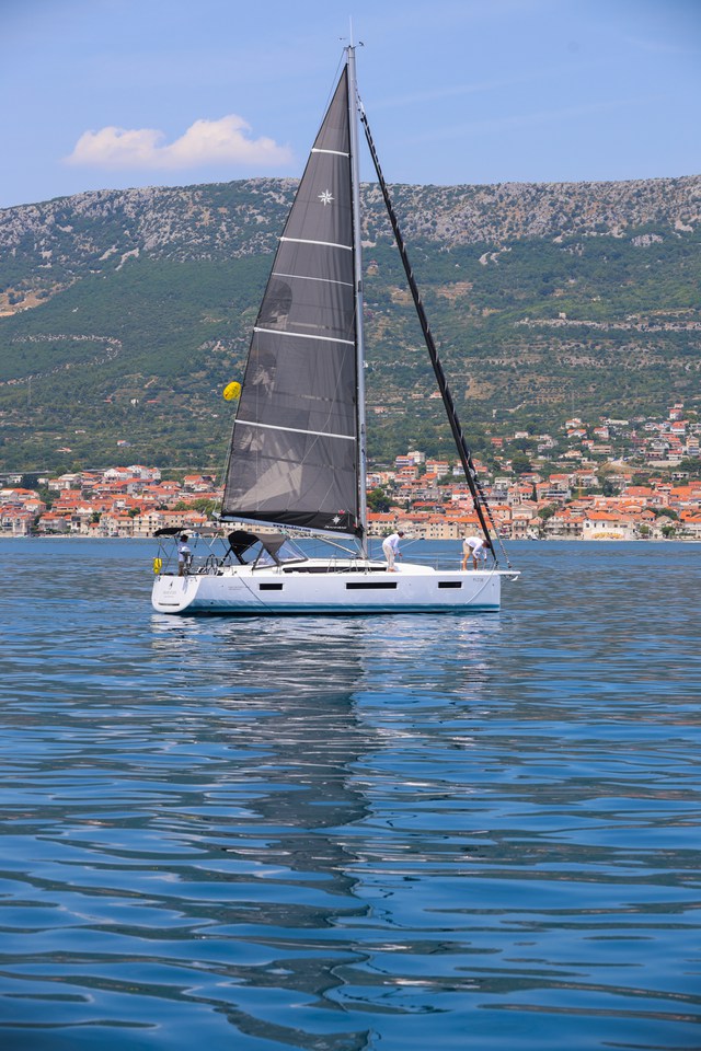Sleek profile of Dreamcatcher gliding through tranquil waters with a picturesque coastal backdrop.