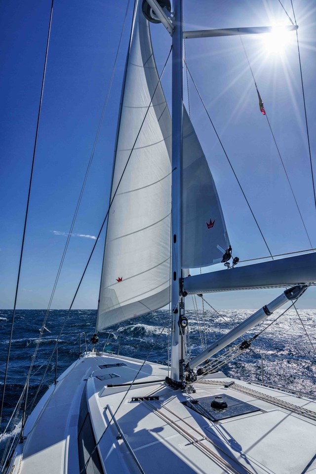 Sailing Ostwind II with billowing sails against a bright blue sky and ocean waves.