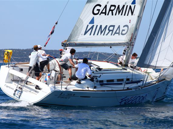 Sailing yacht Aquarius gliding through azure waters with crew adjusting sails.
