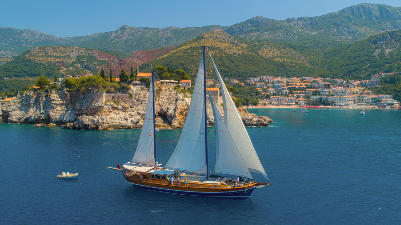 Kaptan Sevket gracefully sailing along a picturesque coastline with majestic mountains in the background.