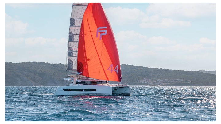 CinSéLuna gliding gracefully through vibrant waters, showcasing its striking red sails against a scenic backdrop.