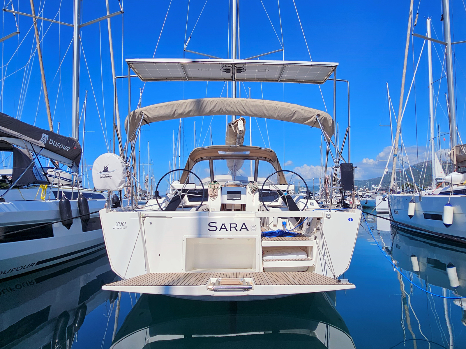 Sleek profile of the luxury yacht Sara docked in a vibrant marina under clear blue skies.